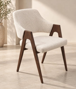 A modern armchair with a cream upholstered seat and back, dark walnut wooden frame, tapered legs, and sculptural open arms.