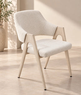 A modern armchair with a cream upholstered seat and back, BEIGE wooden frame, tapered legs, and sculptural open arms.