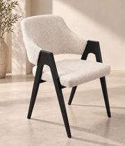 A modern armchair with a cream upholstered seat and back, BLACK wooden frame, tapered legs, and sculptural open arms.