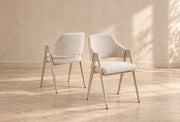 A modern armchair with a cream upholstered seat and back, BEIGE wooden frame, tapered legs, and sculptural open arms.